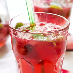 A glass of The Raspberry Julep garnished with Fresh Mint Leaves and fresh Raspberries and  a straws