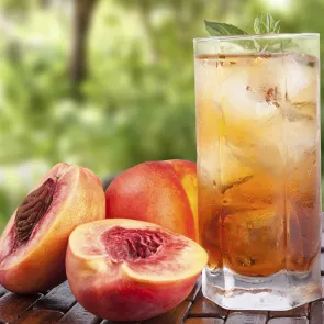 A glass of Front Porch Peach Tea with a peach and half a peach on the side, refreshing and fruity.