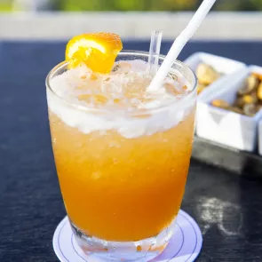 Glass of Kentucky Sunrise with ice, strrir and straws garnished with lemon slices