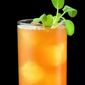 a glass of Apricot Sage Bourbon Cocktail garnished with ice and sage leaves