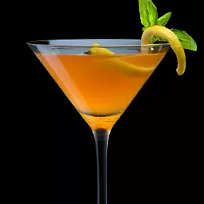 Glass of Citrus Basil Manhattan garnished with a lemon twist and basil leaves.