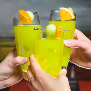 Three person cheersing with glass of Fuzzy Melon Ball garnished with orange slice and melon ball