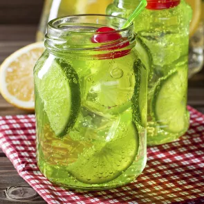 Two jars of Midori® Mistletoe with lime wedges on a red checker ed napkin, garnished with a cherry.