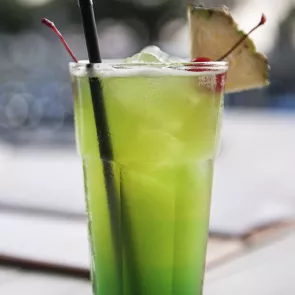 Glass of Midori® Splice with  straws, garnished with a cherry and pineapple.