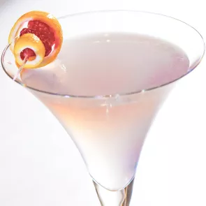 A martini glass of Chocolate Covered Berries, garnished with a stick featuring a lemon peel and raspberry.