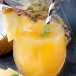 A glass of Coconut Spritzer, garnished with a pineapple slice, mint leaves and straws.