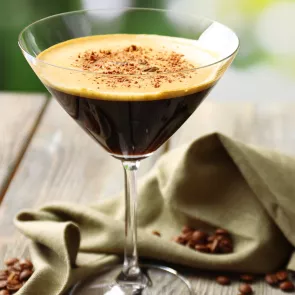 A cocktail glass of Mocha Razz-Tini garnished with powdered chocolate, alongside a napkin, placed with some powdered chocolate spread nearby.