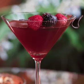 A cocktail glass of Pineapple Razztini, garnished with a pineapple slice and raspberry on a cocktail pick.