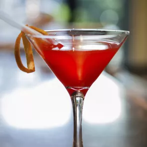 A martini glass of Red Greyhound Pinn-Tini garnished with an orange slice and a straw in it.