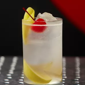 A glass of Juan Collins garnished with lemon peel, Cherry and ice cubes