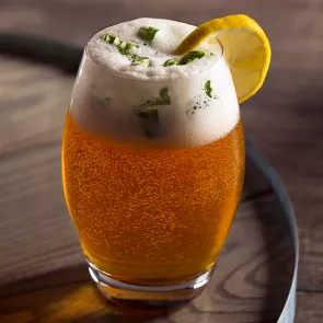 Glass of Beam and Hops garnished with a lemon slice and basil leaves.