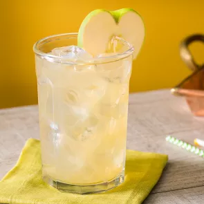 A glass of Crisp Apple Ade garnished with green apple slice on green coaster