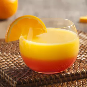 A cocktail glass of Sunrise, adorned with an orange slice, rests elegantly on a coaster.