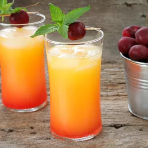 Two glasses of Cruzan® 9 Punch garnished with cherry and mint leaves alongside bucket of cherries