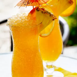 A glass of Classic Rum Punch garnished with crushed ice, orange and pineapple slices, and a cocktail umbrella on the rim of the glass.