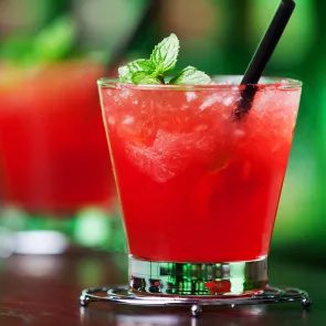 Glass of Berry Burst with straws garnished with mint leaves on steel coaster