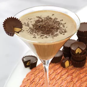 Glass of Peanut Butter Cup Martini garnished with Peanut Butter Cup alongside few Peanut Butter Cups