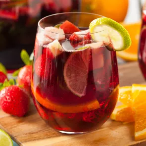 1.A glass of Razzmatazz® Sangria garnished with  chopped fruits and a lemon slice on a rim along side few strawberries and orange slices