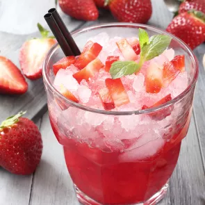 Glass of strawberry Margarita garnished with crushed ice, strawsberry pieces, mint leaves and straws