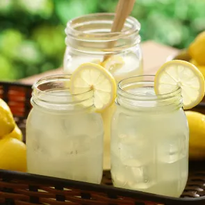 Two jars of Jim Beam® Lemonade garnished with lemon slice in a basket alongside few lemons