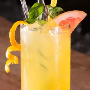 a glass of Apricot Sour garnished with a slice of grapefruit, basil leaves and orange twist