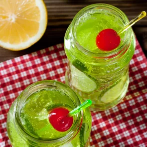 Two Jar of Midori® and Ginger garnished with a cherry on a napkeen alongside  a half orange.