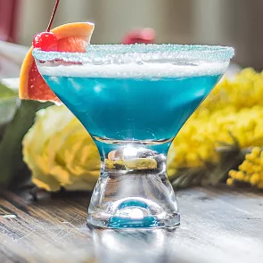 A cocktail glass of Sauza® Blue garnished with blood orange slice and cherry with crushed sugar rim.