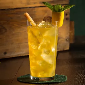 Glass of David Beam's 1838 Cocktail on a coaster, garnished with a sugar cane stir stick and a pineapple parrot.