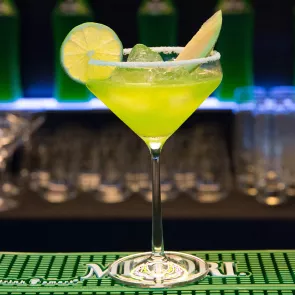 A cocktail glass of Midori® Margarita garnished with a lime wedge and wheel with salt rim sits on the table.