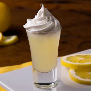 A glass of Ooh La La Lemon topped with whipped cream sits on a coaster, accompanied by lemon slices