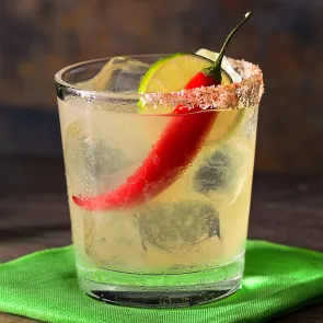 Glass of Samba Margarita garnished with lemon slice and a red chilli on green coaster